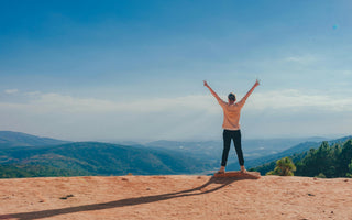 A girl stands at the top of a mountain, celebrating her achievement.