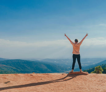 A girl stands at the top of a mountain, celebrating her achievement.