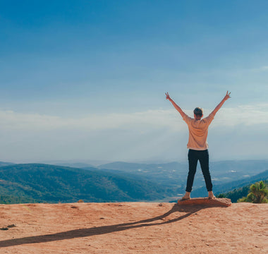 A girl stands at the top of a mountain, celebrating her achievement.
